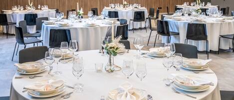 Un salón de banquetes con mesas redondas dispuestas para cenar, con manteles blancos y sillas negras.