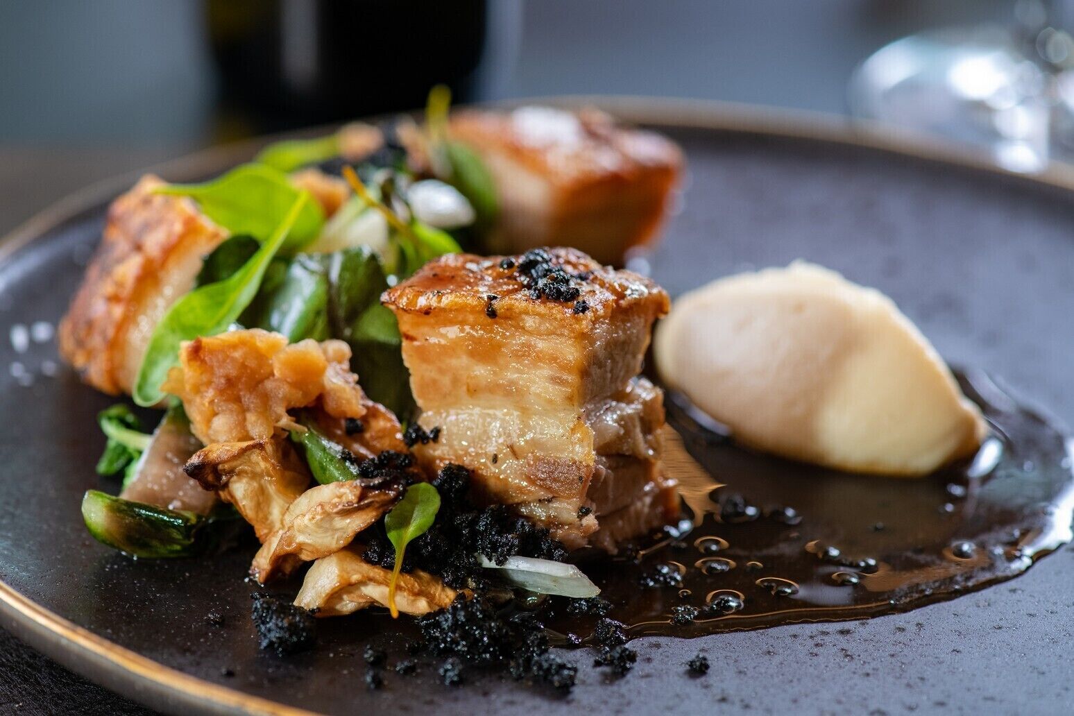 A plate of food with pork, greens, and a dollop of sauce.