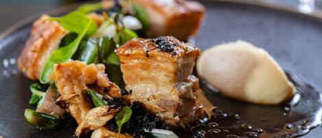 A plate of food with pork, greens, and a dollop of sauce.