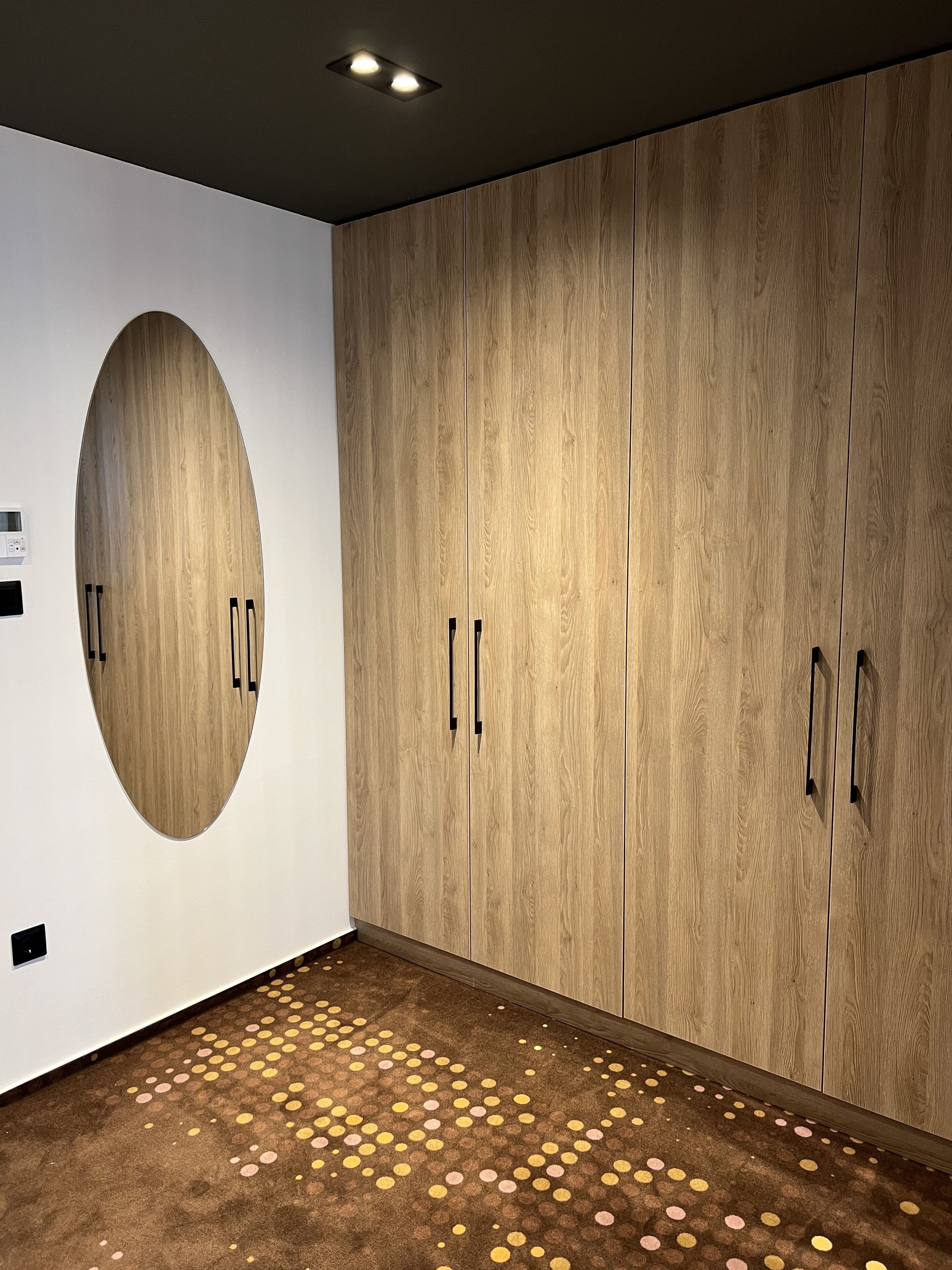 A room with a wooden wardrobe, a circular mirror, and a patterned carpet.
