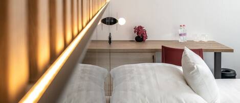A modern bedroom with a bed, bedside table, lamp, and a small desk with a vase of flowers.