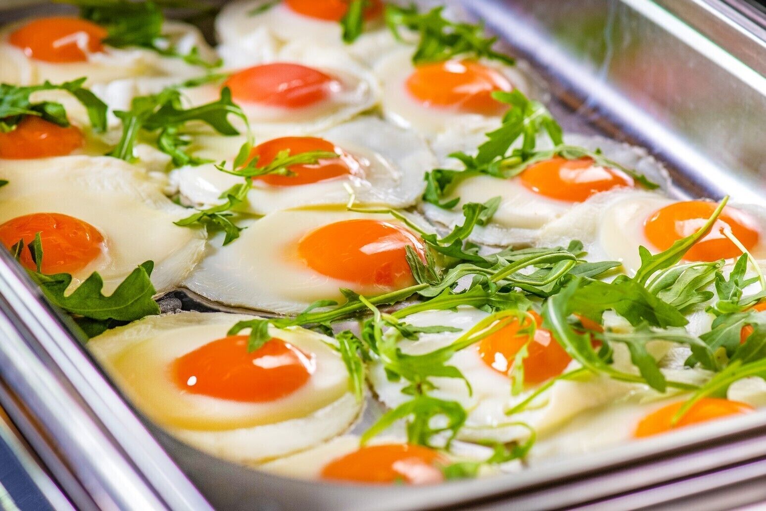 A buffet tray with poached eggs garnished with arugula and cherry tomatoes.