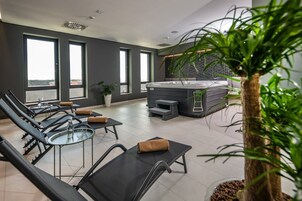 A modern indoor relaxation area with sun loungers, a hot tub, and large windows offering views.