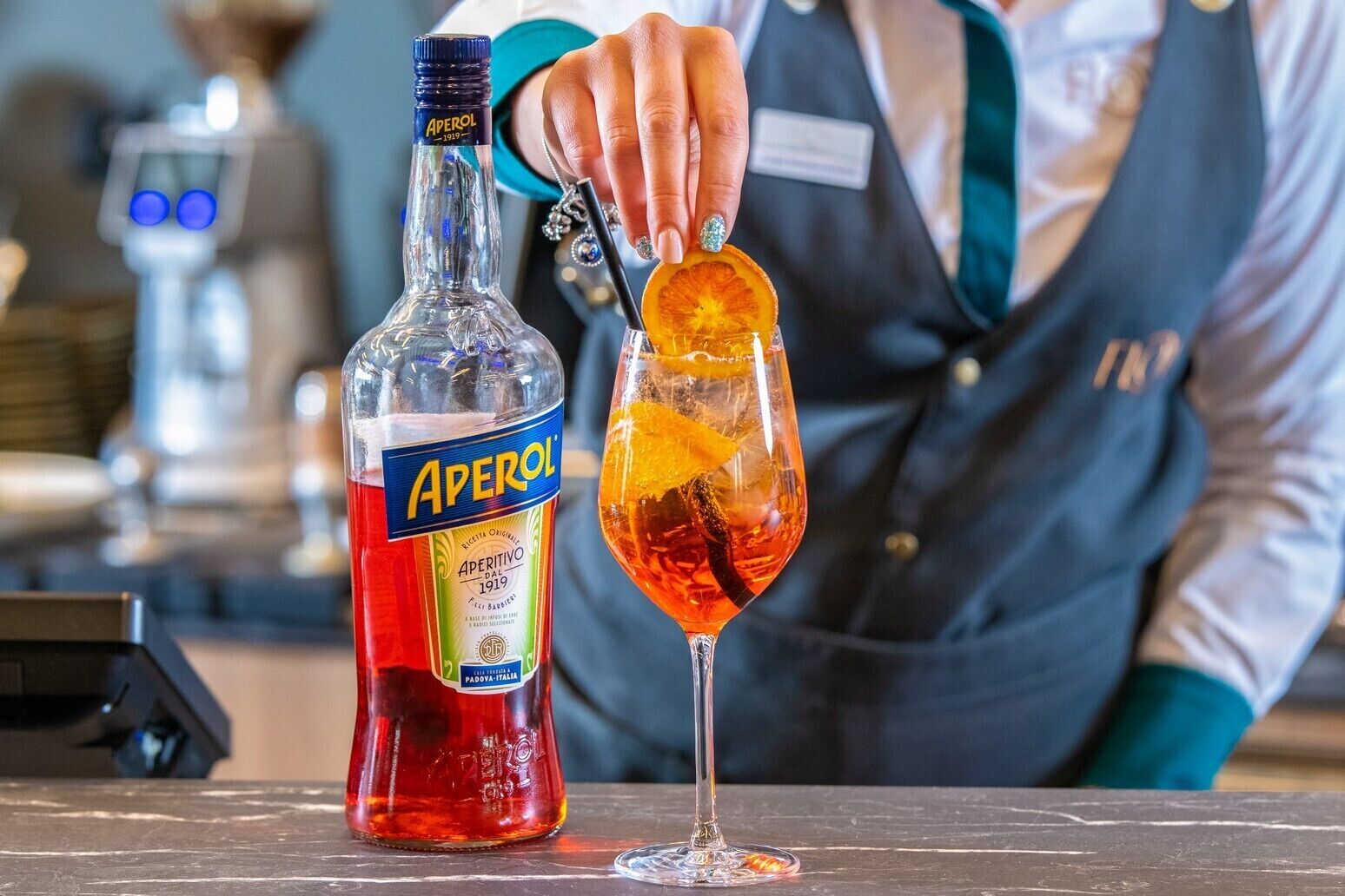 A bottle of Aperol and a cocktail glass with an orange slice on a bar counter.