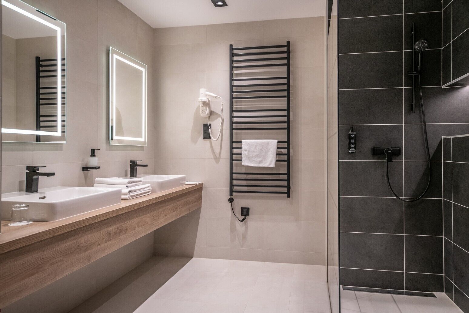 A modern bathroom with two sinks, a towel rack, a heated towel rail, and a shower area.