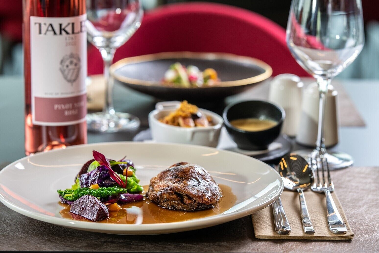 Una mesa de comedor con un plato de comida, una botella de vino y una copa de vino.