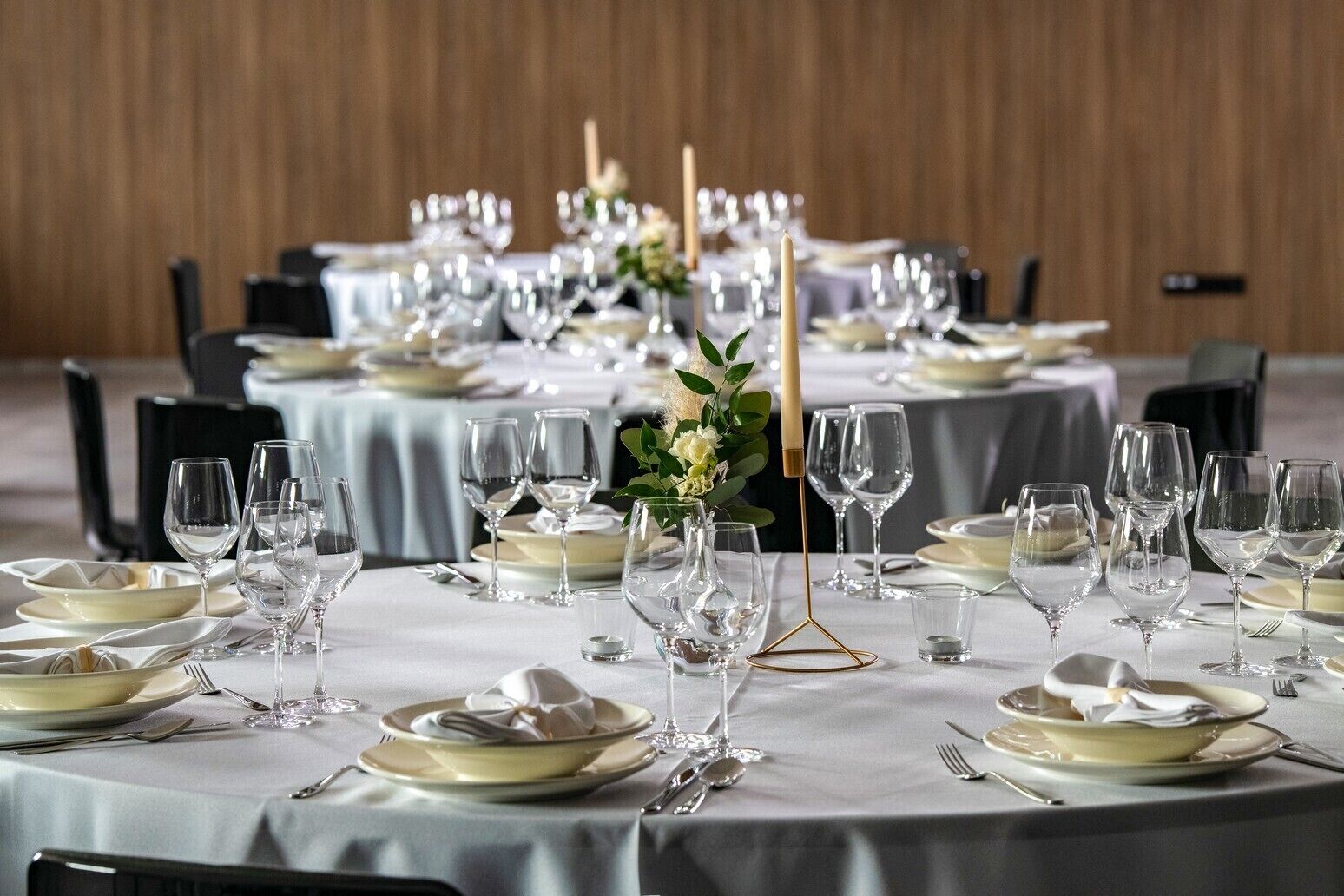 Un salón de banquetes con mesas redondas dispuestas para comer, con manteles blancos, copas de cristal transparente y centros de mesa elegantes.