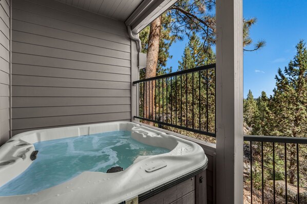 A hot tub on a balcony with a view of pine trees.