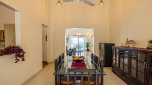 A spacious dining area with a glass table and chairs, a ceiling fan, and a view into another room. - amã Stays & Trails Arcadia, Coorg (Virajpet)