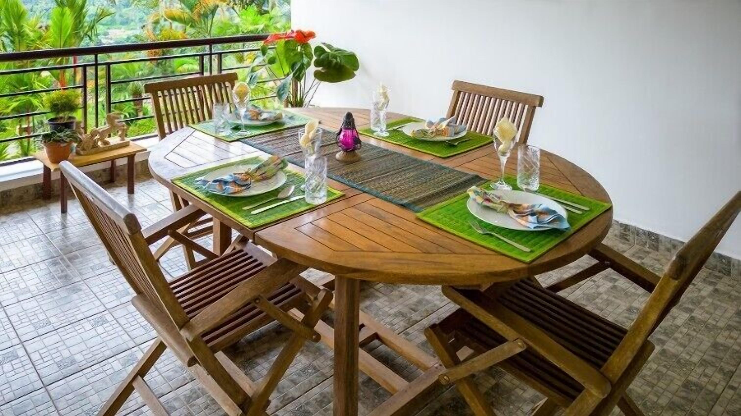 A round wooden table with green placemats, surrounded by wooden chairs.