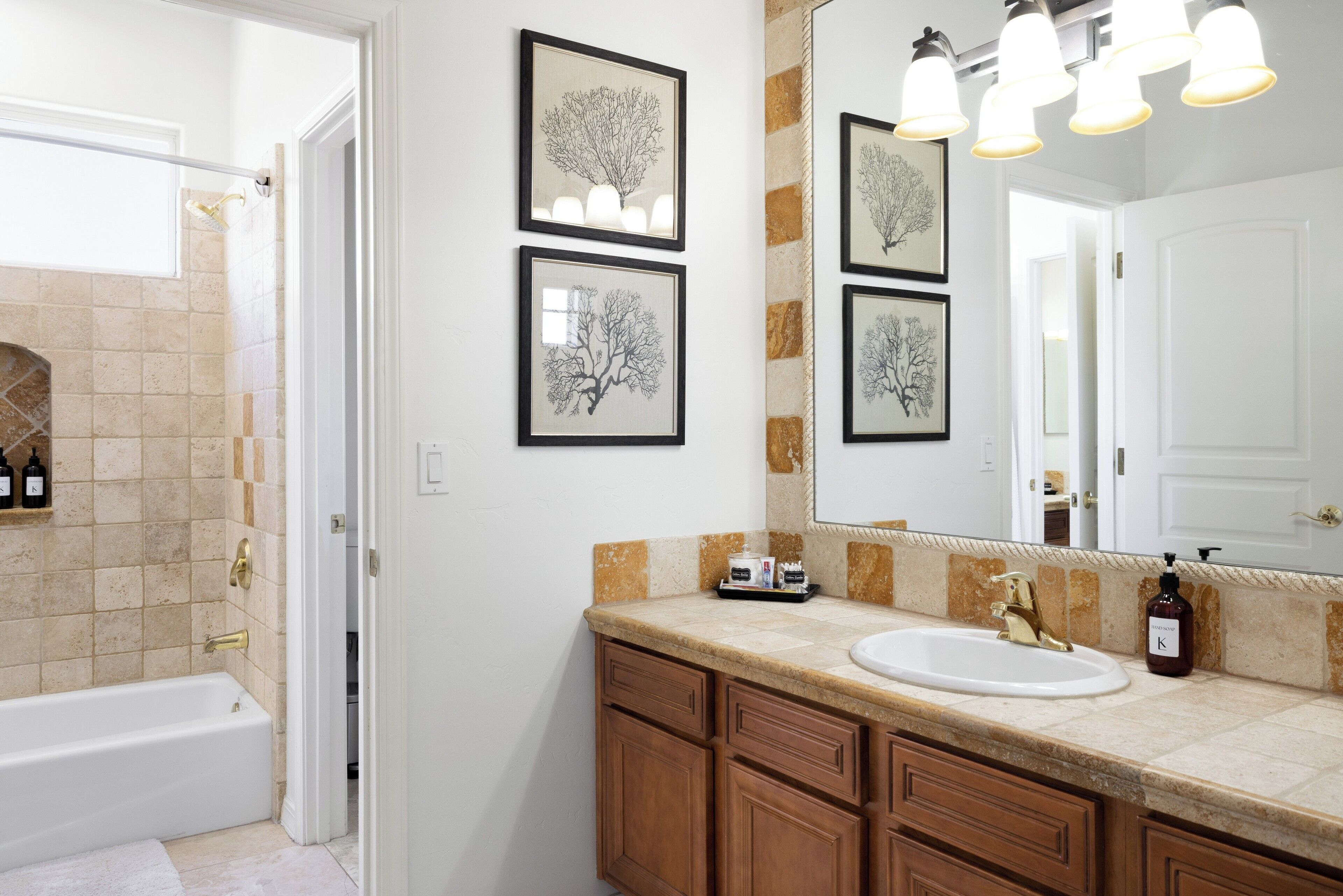 A bathroom with a bathtub, a sink, wooden cabinets, and framed artwork on the wall.
