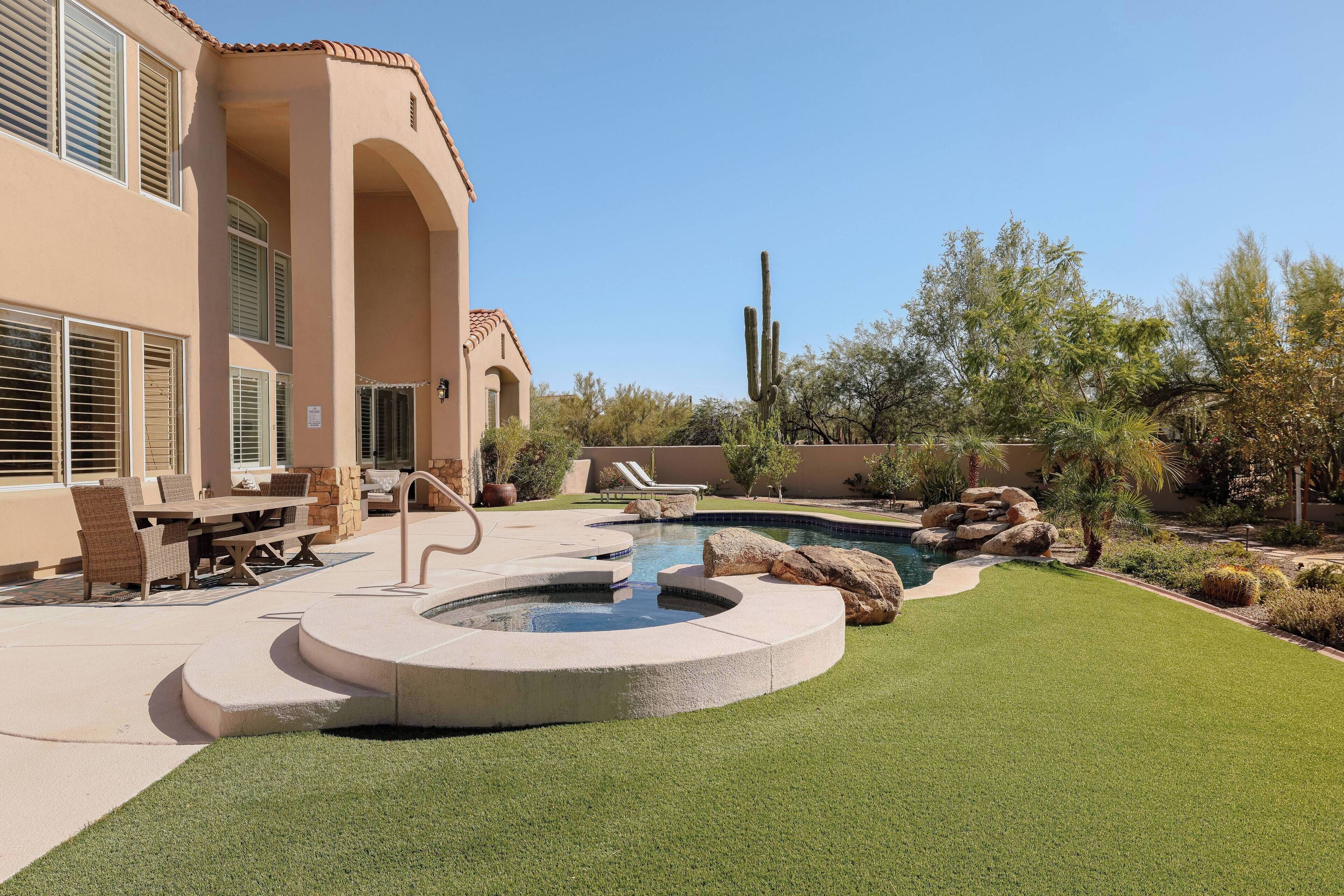 Piscina com hidromassagem, rodeada por um terraço com mobiliário de exterior, numa área ajardinada com cactos e árvores.