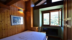A wooden room with a bed, a window with a view of trees, and a fireplace. - Terrace, fireplace or stove, tv, ski locker, 30m², Les Menuires (Saint-Martin-de-Belleville)