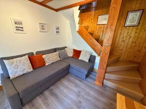 Ein modernes Wohnzimmer mit einem grauen Ecksofa, einer Holztreppe und gerahmten Bildern an den Wänden.