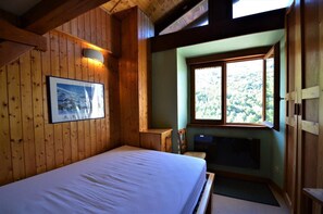 Ein Zimmer mit Holzboden, einem Bett, einem Fenster mit Blick auf Bäume und einem gerahmten Bild an der Wand.