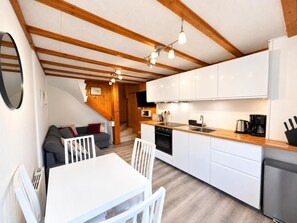 Une cuisine compacte avec des meubles blancs, un plan de travail en bois et un coin repas comprenant une table et des chaises blanches.