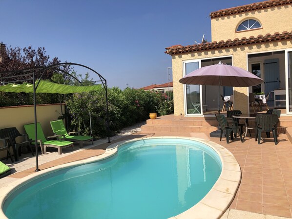 Piscina com espreguiçadeiras verdes e mesa de apoio com cadeiras.