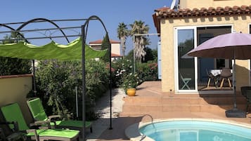 Une piscine avec des chaises longues, une pergola et un espace patio comprenant une table et des chaises.