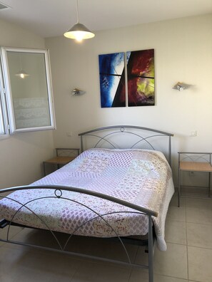 Quarto com cama, janela, luminária na parede e duas mesas de cabeceira.