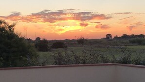 A balcony with a table and chairs, overlooking a field with sparse vegetation and a sunset sky. - 5'du Barcares, lovely air-conditioned villa with heated pool (ST LAURENT DE LA SALANQUE)