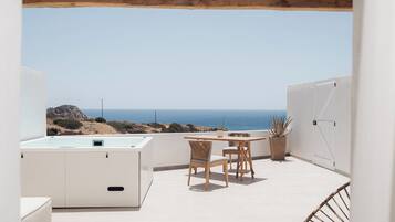 Una terraza en la azotea con una pérgola de madera, una mesa con sillas, una planta en maceta y vistas al mar.