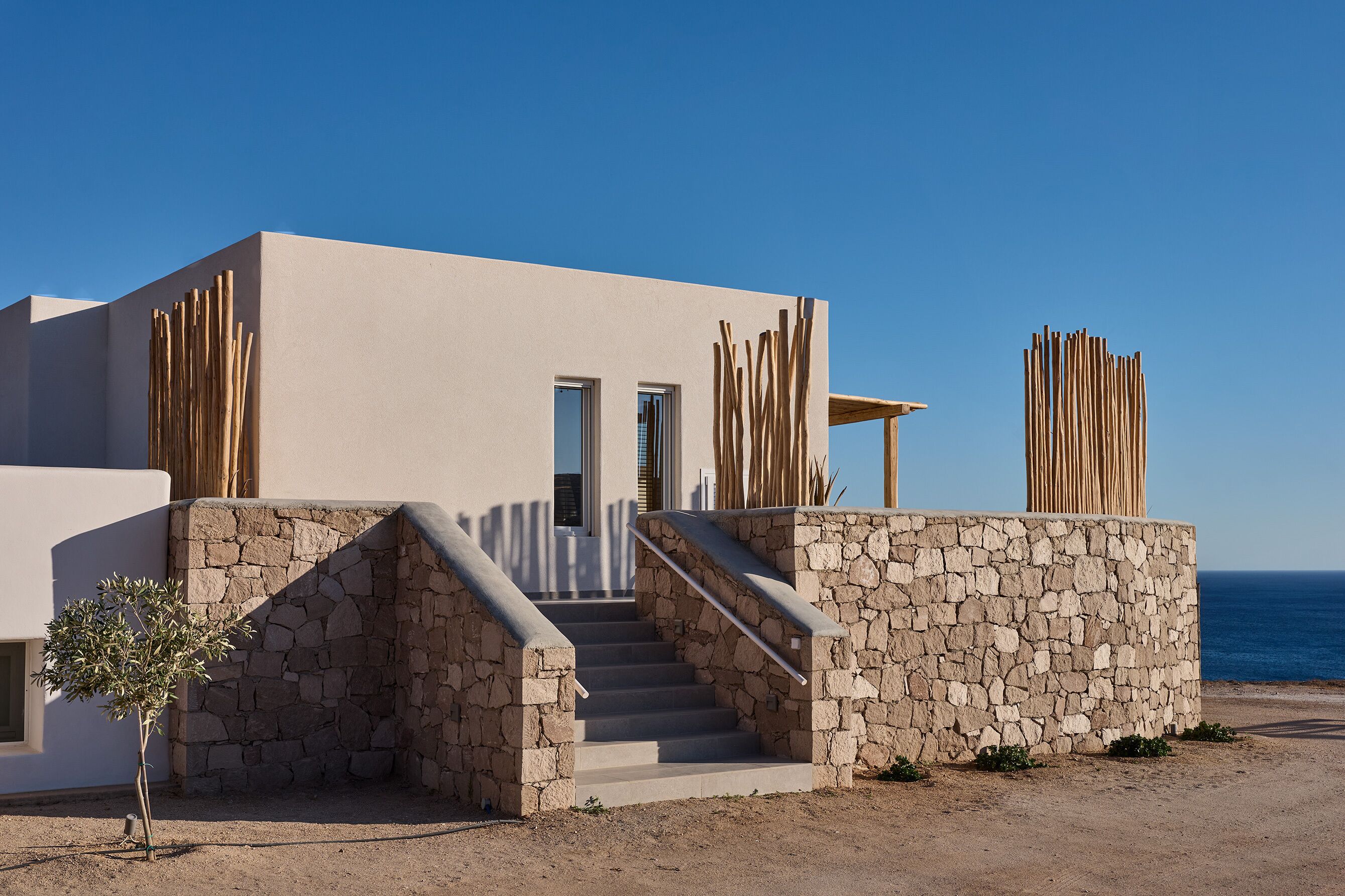A modern building with a stone facade, a staircase leading to a door, and a view of the sea.