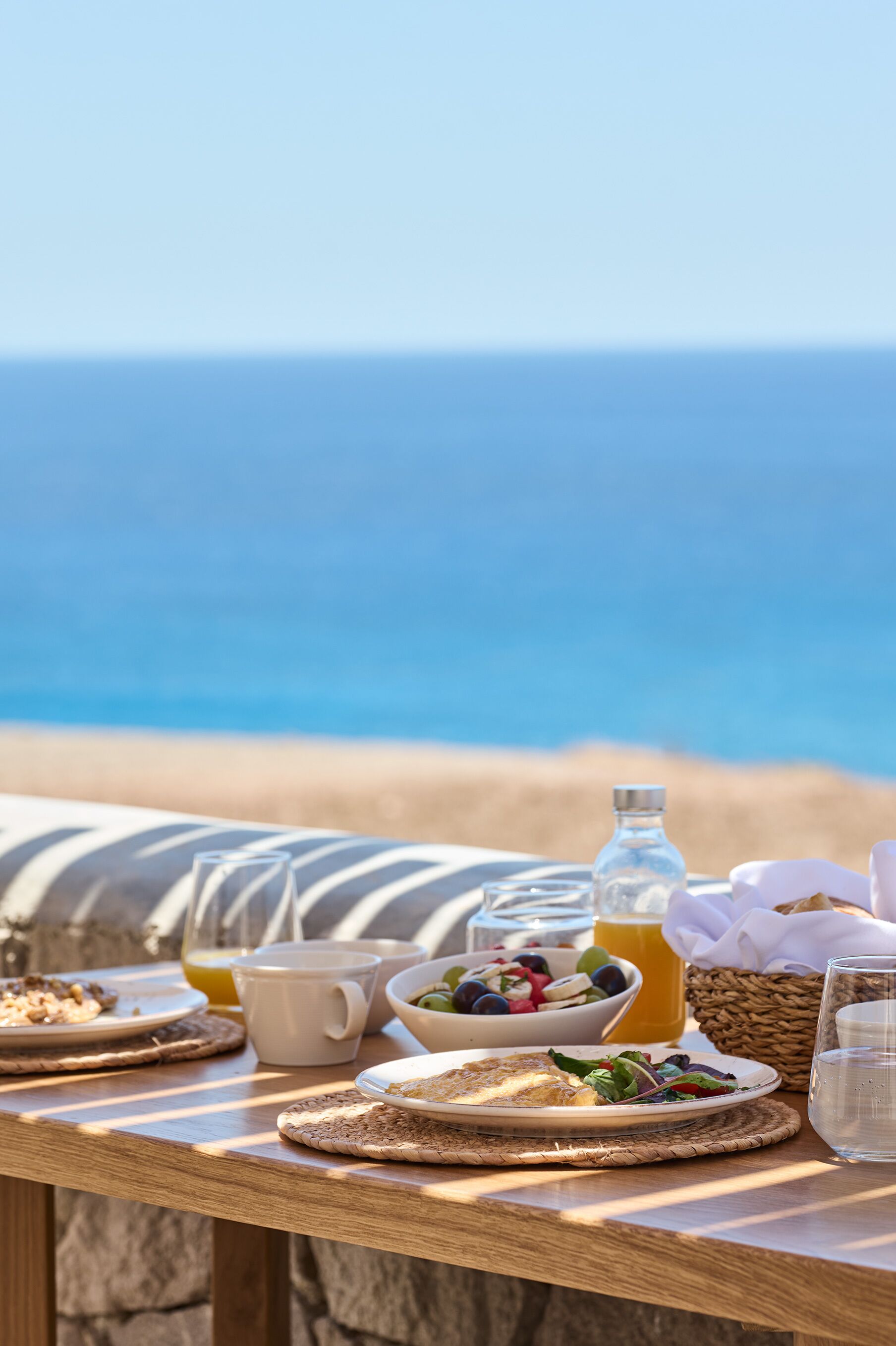 Une table avec des aliments pour le petit-déjeuner, un verre d’eau et une vue sur l’océan.