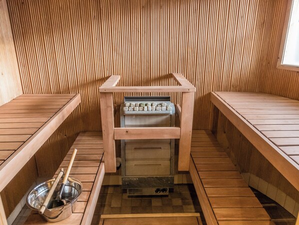 A sauna room with wooden benches, a bench with a towel rack, and a metal basin with a wooden handle.