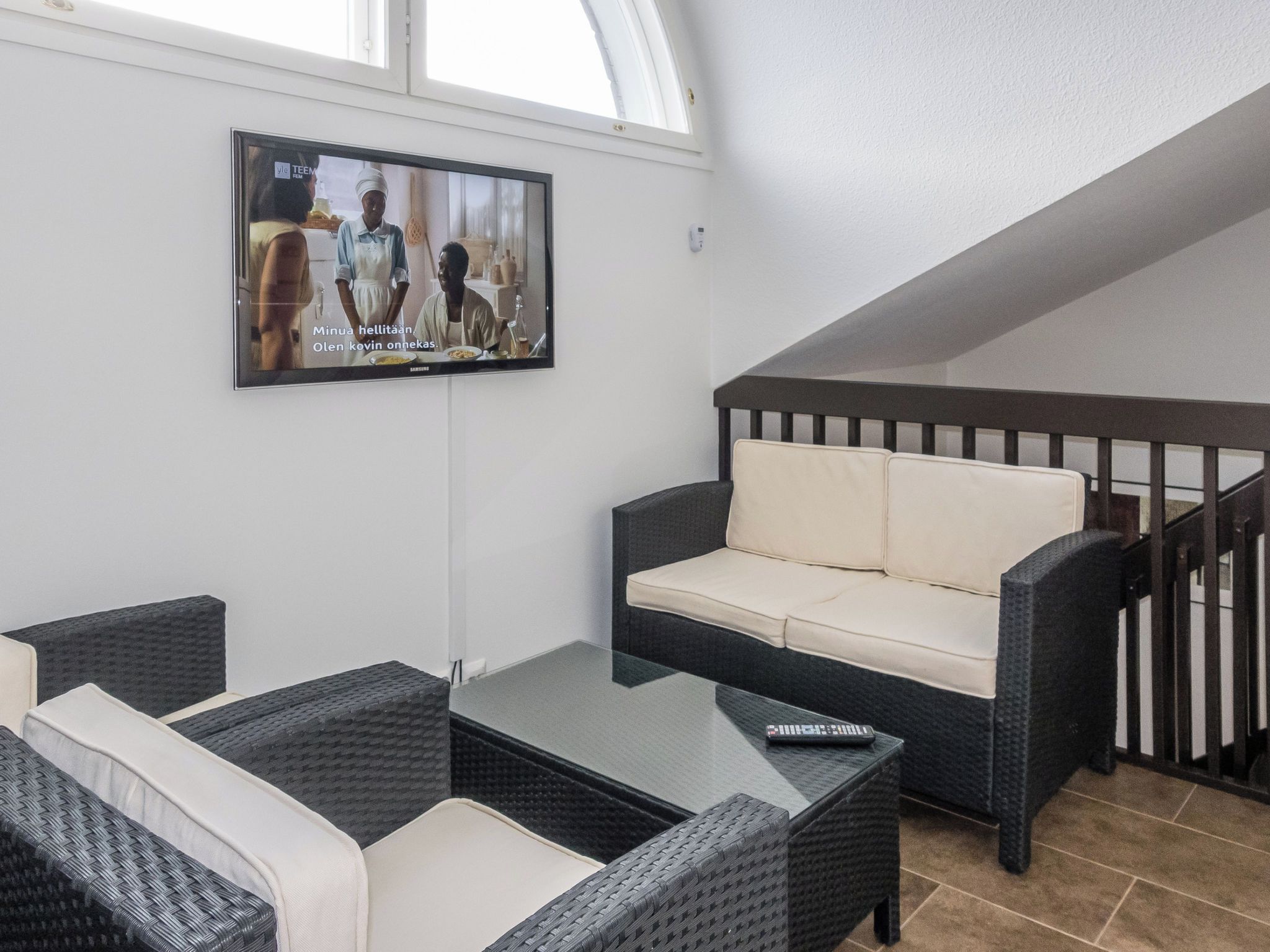 Una sala de estar moderna con un sofá, dos sillones, una mesa de centro y un televisor de pantalla plana montado en la pared.