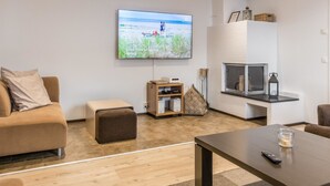 Uma sala de estar moderna com uma televisão de tela plana, um sofá, uma mesa de centro e um pequeno banquinho.