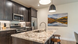 A modern kitchen with dark wood cabinets, stainless steel appliances, a granite countertop, and a large island with a sink. - In the Heart Of Keystone, Mountain Views from Private Balcony! (Keystone)