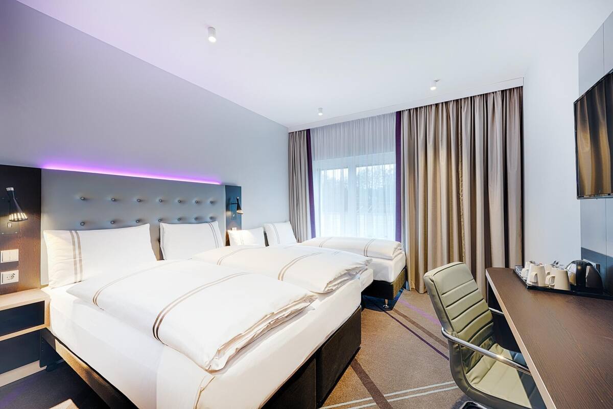 Habitación de hotel con una cama grande, un escritorio con silla, un televisor de pantalla plana y una ventana con cortinas.
