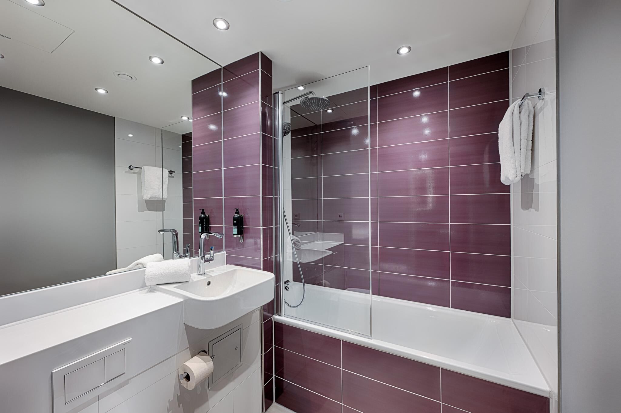 Een moderne badkamer met een grote spiegel, twee wastafels, een douche en een toilet.