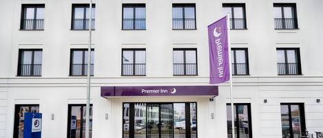 A hotel entrance with a prominent 'Premier Inn' sign, a flag, and a blue information board.