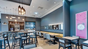A modern cafe with a breakfast bar, seating area, and a large poster on the wall. - Premier Inn Regensburg City Centre (Regensburg)