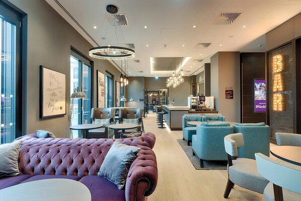A modern hotel lobby with a plush seating area, a bar, and a reception desk.