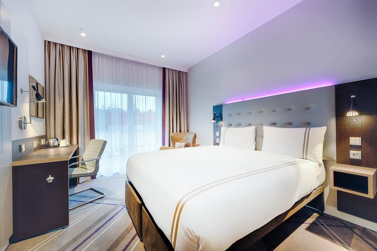 Habitación de hotel con una cama grande, un escritorio, una silla y vistas a la ciudad.