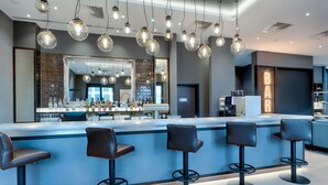 Un área de bar moderna con una barra larga, varios taburetes y lámparas colgantes.