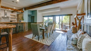 A spacious dining area with a wooden table and chairs, a kitchen in the background, and a view of the outdoors through large windows. - Lakefront Estate With 2 Kitchens Perfect for Events & Families (Nevada)