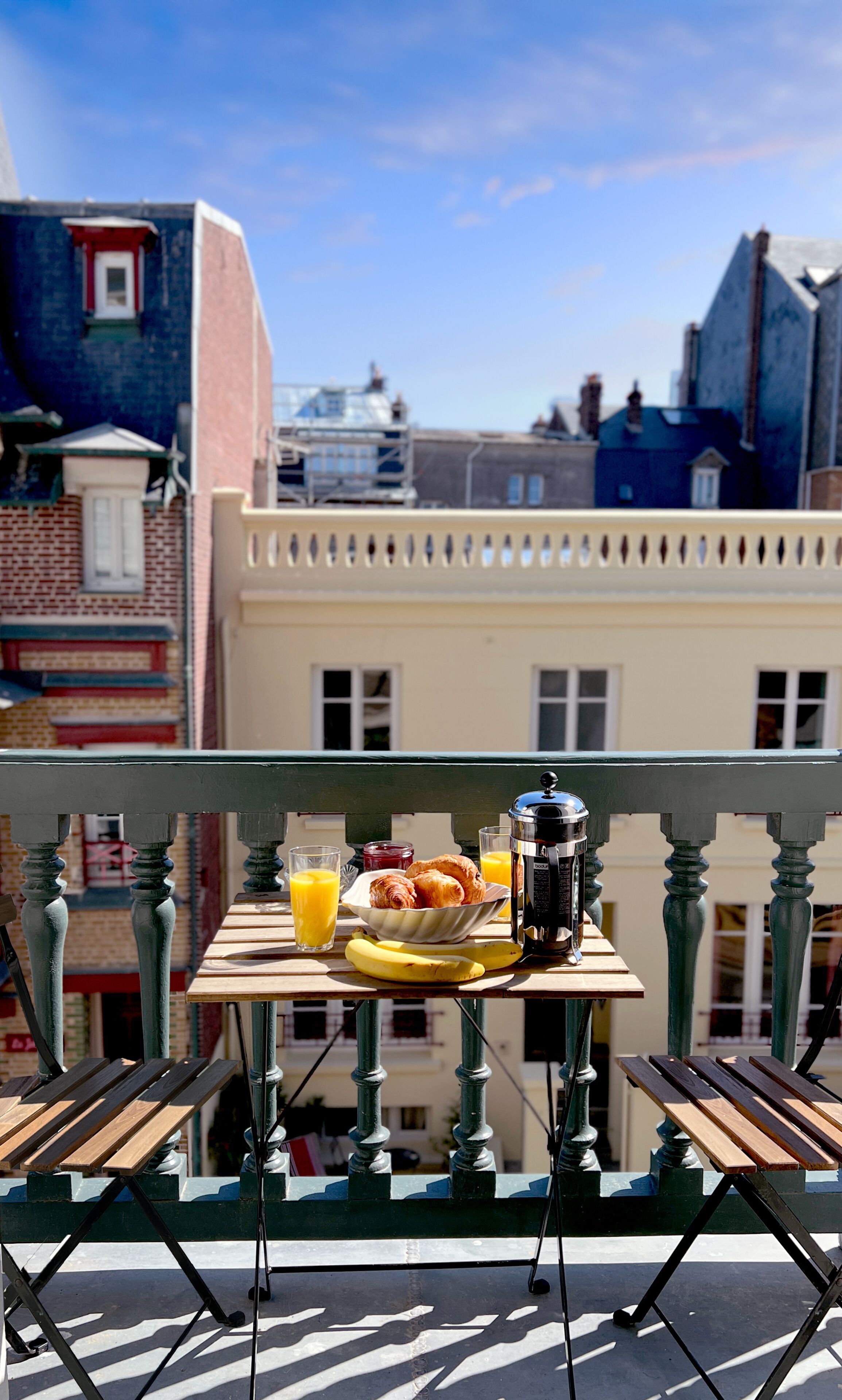 Ein Tisch mit Frühstücksangeboten und Getränken auf einem Balkon mit Blick auf die Stadt.
