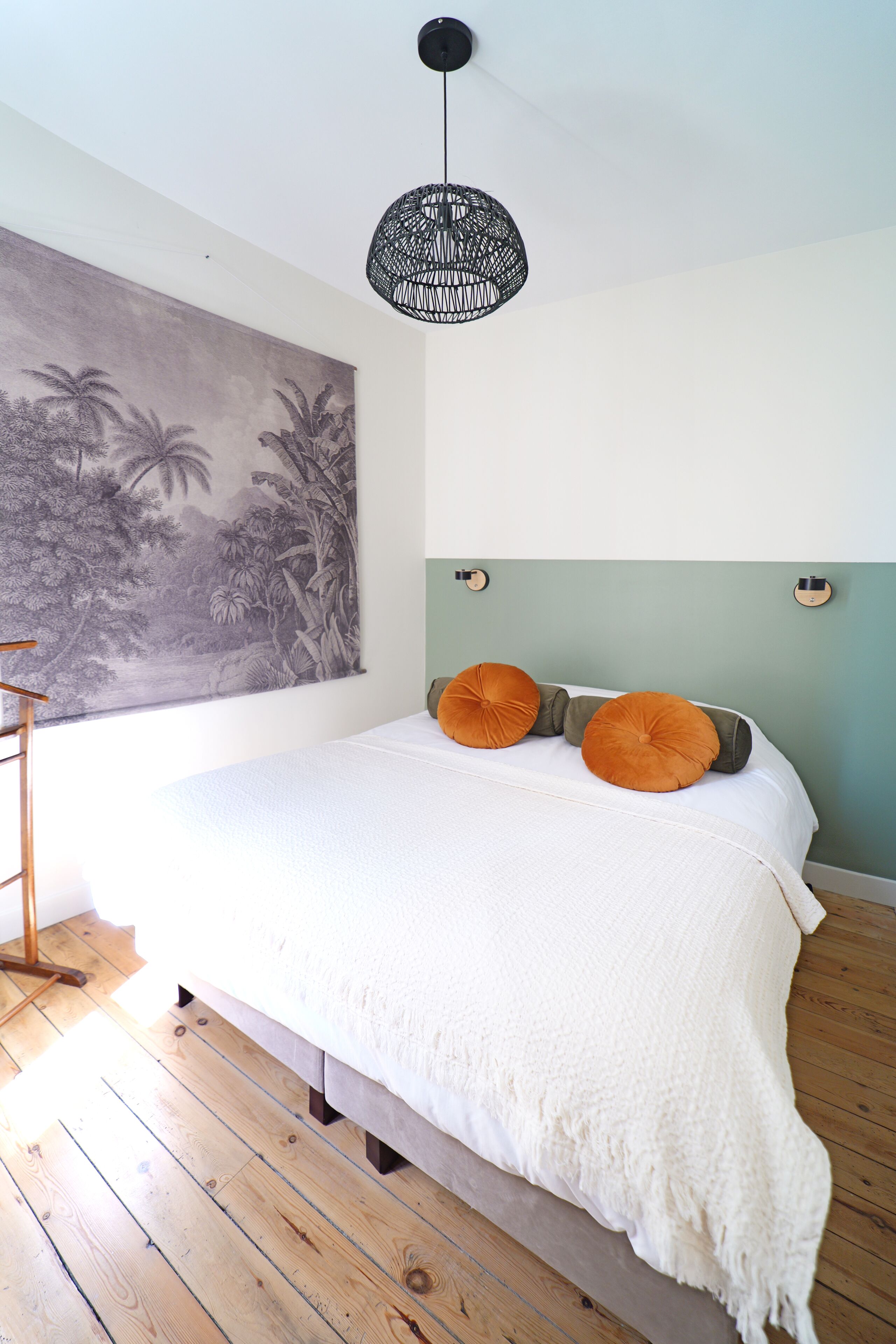Ein Schlafzimmer mit einem Bett, einem großen Wandbild, einer Hängelampe und Holzdielen.