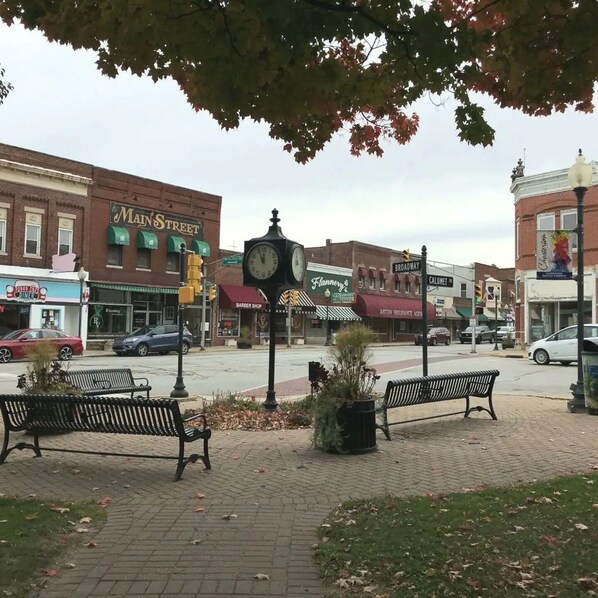 A downtown street with benches, a clock, and various storefronts including a diner and a barber shop.