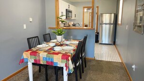 A dining area with a table set for four, a potted plant, and a kitchen in the background. - Private Downtown Apt, King Bed, Jet Bath, Fireplace, Grill, near Indiana Dunes (Chesterton)