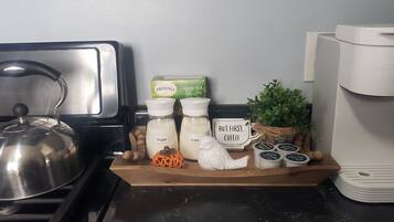 A kitchen counter with a kettle, sugar and creamer containers, Twinings green tea box, a coffee maker, and a small plant.