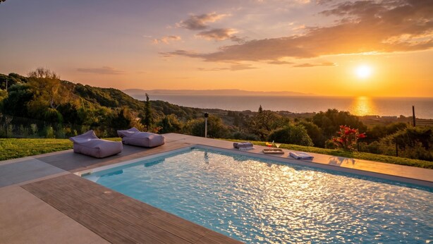 Una piscina con sillas de descanso, vista al atardecer y una masa de agua distante.