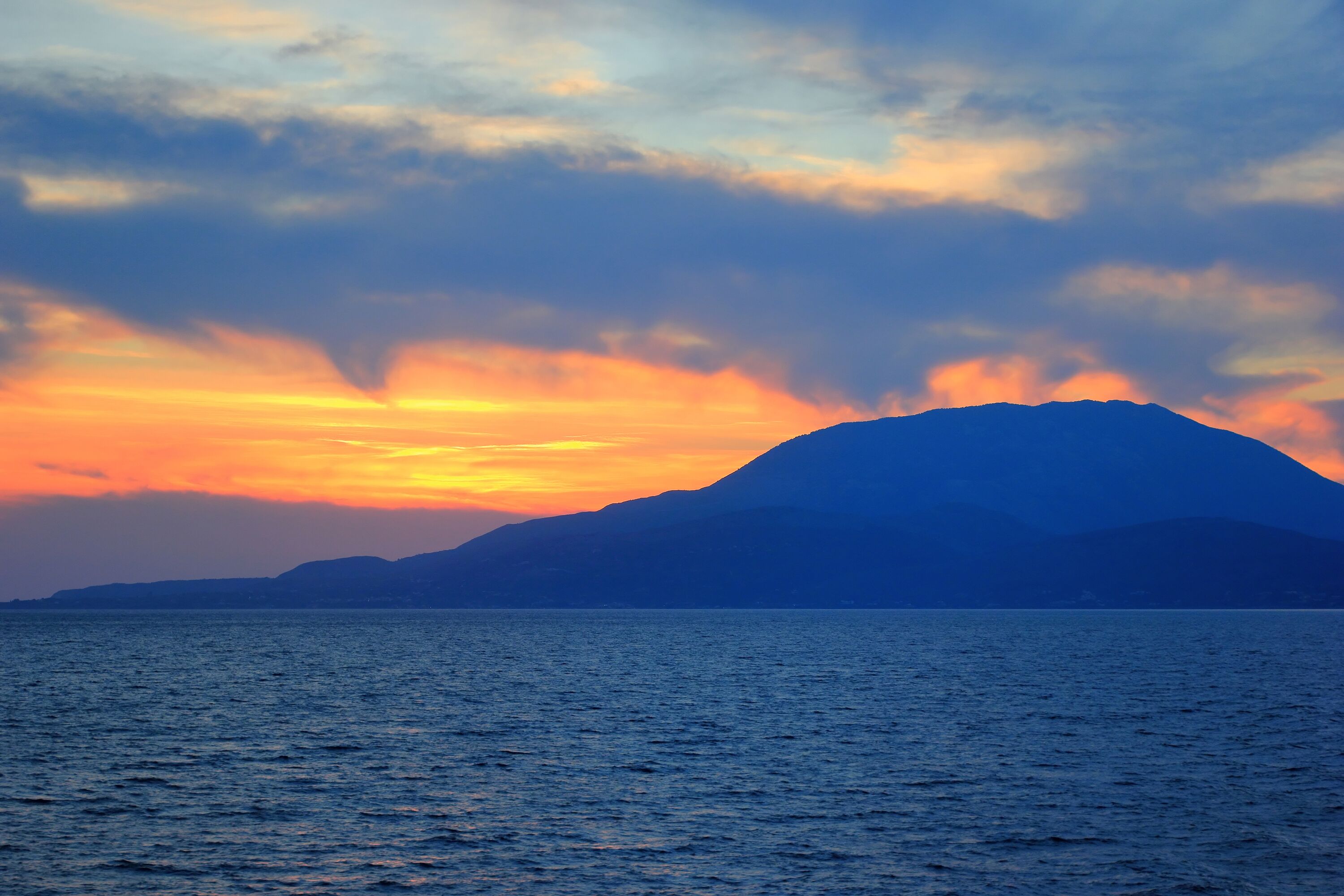 La silhouette d’une montagne se découpant sur le ciel au coucher du soleil, au-dessus d’une mer calme.
