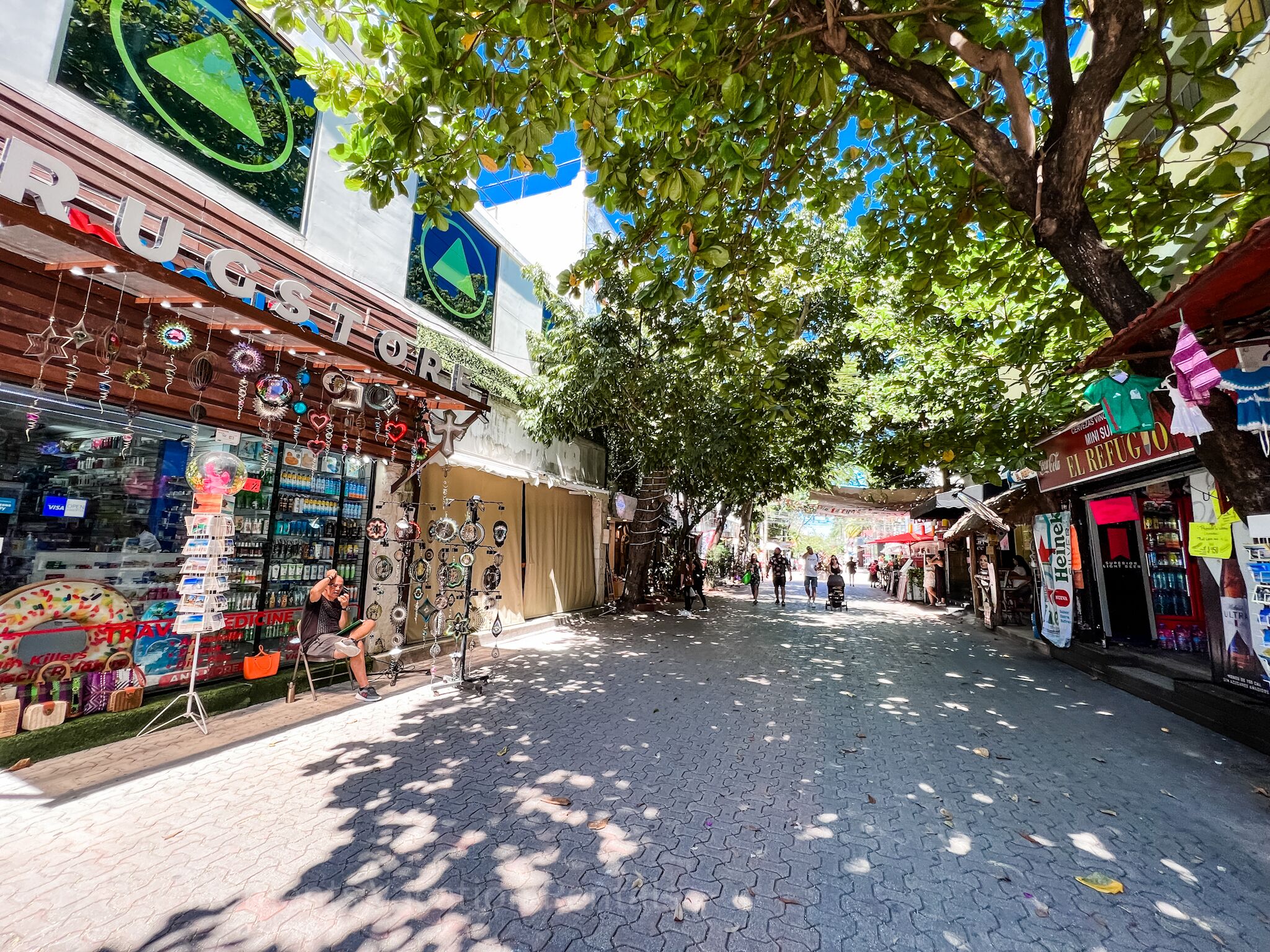 A street with shops, including a pharmacy and a store with a sign that says "El Refugio".