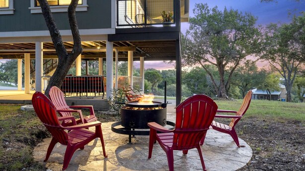 A patio area with a fire pit and red chairs, surrounded by a covered deck and a building with large windows. - Treehouse Cottage | 2 Bed, 1 Bath (Canyon Lake)