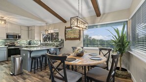 A modern kitchen with a central island, stainless steel appliances, and a dining area with a wooden table and chairs. - Treehouse Cottage | 2 Bed, 1 Bath (Canyon Lake)