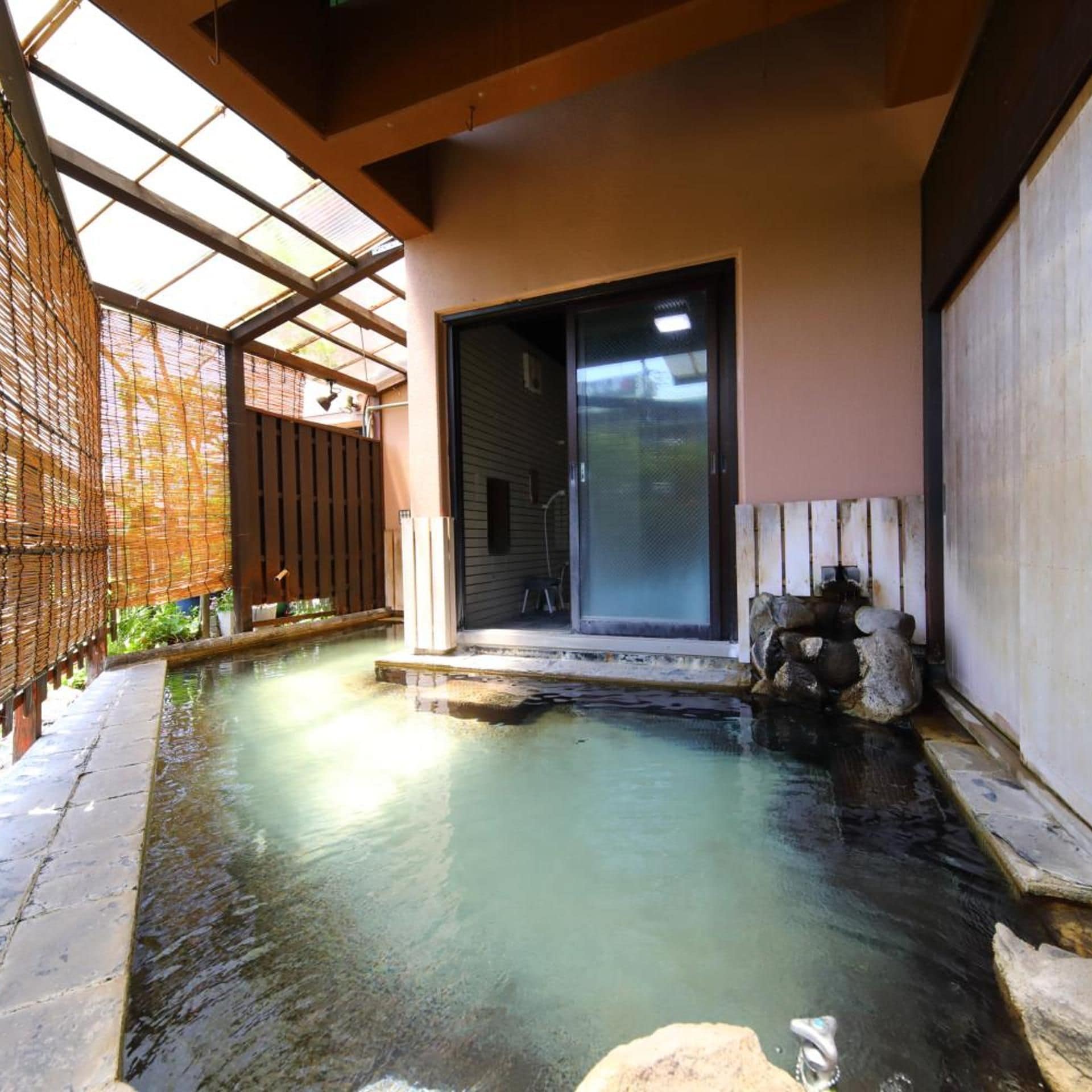 Un onsen japonés tradicional con terraza de madera, bañera de piedra y puerta de cristal que da a la construcción.